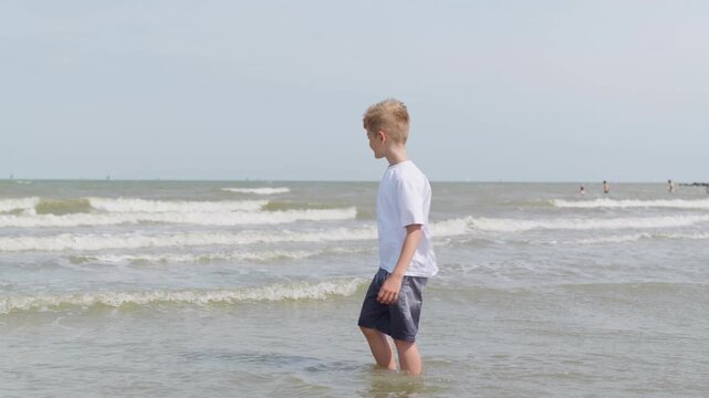 A fully clothed boy is standing in the sea slow motion kneeling in the water