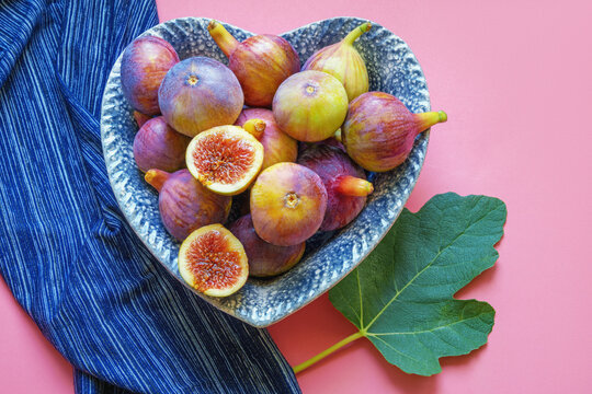 Ripe figs in heart-shaped plate on pink background