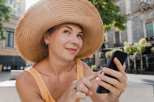 Happy woman in a straw hat using her smartphone outside