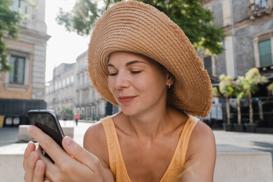 Woman in straw hat using phone in a sunny city square