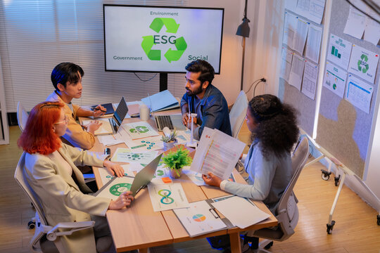 Multiethnic business team discussing ESG sustainability strategy and net zero carbon emission report on screen during meeting with laptops and green documents