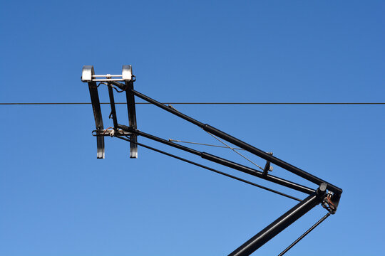 A low angle shot of a black tram pantograph attached to an overhead power line under a clear blue sky.