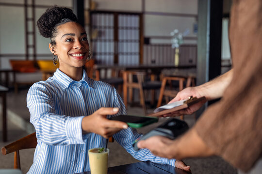 Female customer paying restaurant bill at the table through modern POS terminal