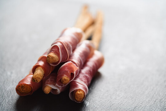 grissini breadsticks with prosciutto on slate background