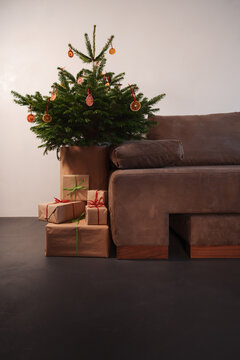Small christmas tree with natural decorations and presents indoor near couch with warm light