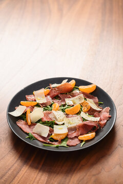 Salad with prosciutto, tangerines and vintage cheese on walnut table with copy space