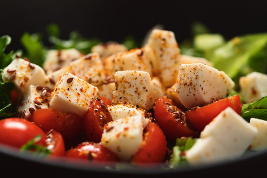 Healthy light salad with cherry tomatoes, mozzarella and frisee in black bowl on walnut surface closeup
