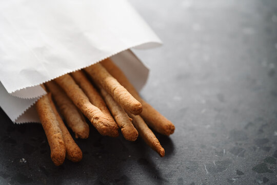 Traditional italian snack - grissini in white paper bag on concrete surface
