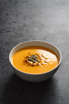 Pumpkin soup decorated with pumpkin seeds oil in white bowl on concrete background with copy space