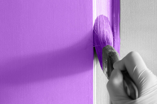 Painting a wooden panel door purple with a paint brush. Do it yourself home decorating project.