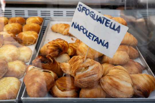 traditional italian Sfogliatella pastries displayed in an Italian bakery case with flaky layers and handwritten sign