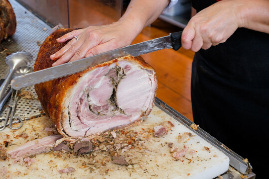 Chef slices porchetta roast with a serrated knife on a cutting board