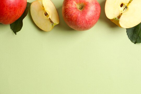 Whole and sliced ​​red apples with green leaves on color background, top view