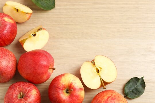 Whole and sliced ​​red apples with green leaves on wooden background, top view