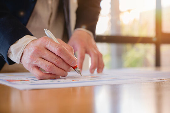 Businessman using pen and paper report while analyzing data at office, Financial analysis or business evaluation concept