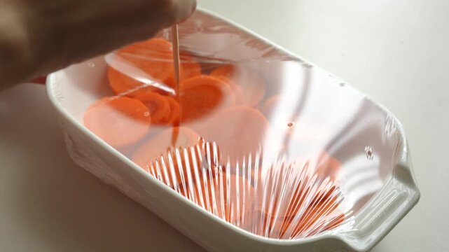 Poking small holes in plastic wrap covering a dish of carrots with a toothpick before steaming