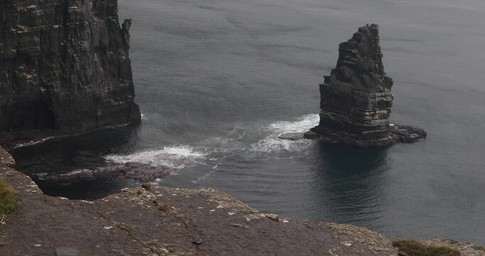 Branaunmore sea stack rises from the Atlantic at Ireland&rsquo;s Cliffs of Moher, displaying dramatic layered rock formations as waves break around its base beneath an overcast sky.