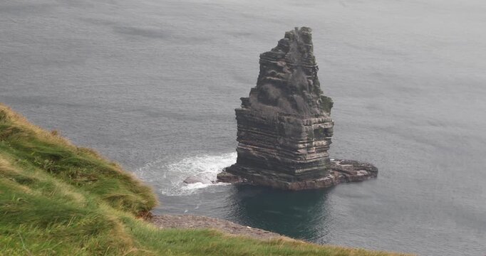 Branaunmore sea stack rises from the Atlantic at Ireland&rsquo;s Cliffs of Moher, displaying dramatic layered rock formations as waves break around its base beneath an overcast sky.