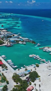 Panoramic aerial landscape of inhabited tropical island surrounded by vibrant turquoise coral reefs. Concept of island geography, marine ecology, and coastal living.Himmafushi.Maldives.Vertical video