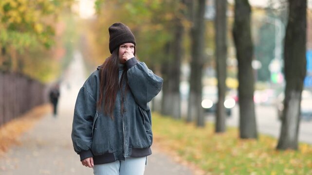 Young woman covers her nose beside busy autumn traffic to avoid exhaust fumes. Vehicle emissions highlight urban air pollution and unpleasant roadside odors.