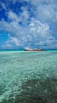 Drone shot of an old abandoned vessel grounded in clear blue water near coral reef. Scenic tropical island background for travel documentary or summer vacation video.Vertical video