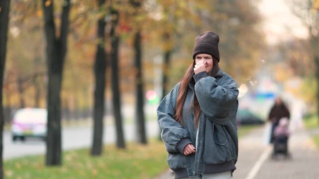 Pregnant woman covers her nose near busy autumn traffic to avoid exhaust fumes. Heightened smell sensitivity and nausea highlight early pregnancy discomfort in polluted cities.