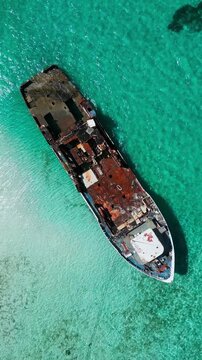 Drone shot of an old abandoned vessel grounded in clear blue water near coral reef. Scenic tropical island background for travel documentary or summer vacation video.Vertical video
