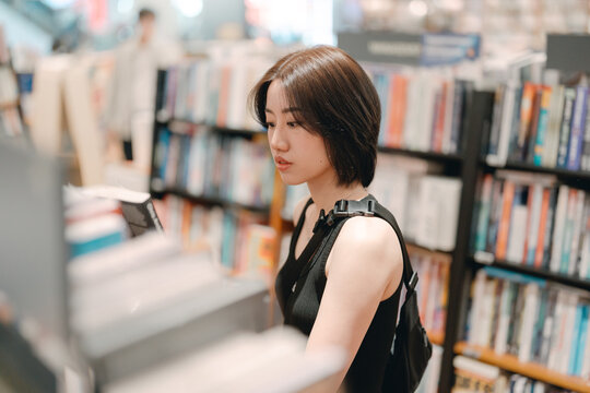 Adult asian woman reading book at bookstore shop choosing from bookshelf