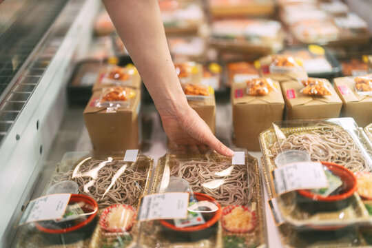 Adult asian single woman customer choosing ready meals cooked food from shelf at asia supermarket