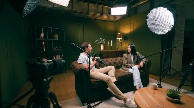 Man and woman recording a live streaming show, having a conversation and interviewing a guest in a professional studio with microphones
