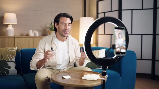 Handsome caucasian man influencer recording a vlog on his smartphone, talking about men's cosmetic products and sharing beauty tips