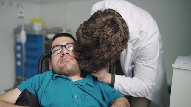 Young man with a disability undergoing a routine otoscopy exam by a specialist in a clinic. Doctor using an otoscope for diagnosis