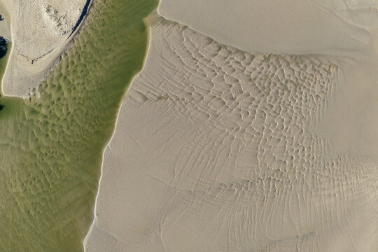 Aerial view looking straight down at shallow green water beside rippled tidal sand at Moonee Creek, Moonee Beach, creating an abstract coastal texture.