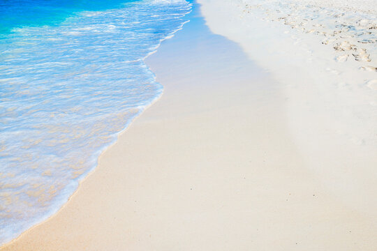 Close-up view of Caribbean Sea waves washing over sandy shoreline with footprints on beach. Aruba.