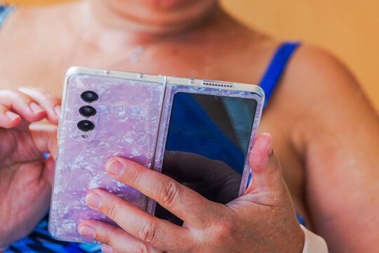 Close-up view of woman sitting on beach while using foldable smartphone in pearlescent protective case. Aruba.