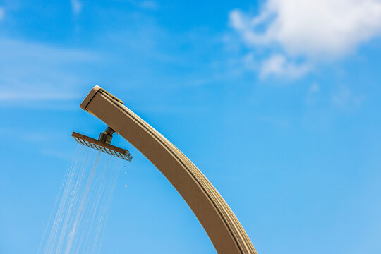 Close-up view of water flowing from beach shower against background of sunlit sky with soft clouds. Aruba.