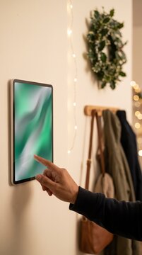 Homeowner tapping a wall mounted smart panel in a decorated entryway with wreath and coats