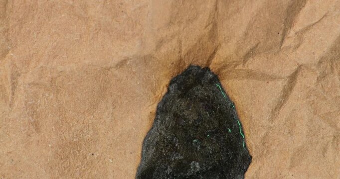 Burning Crumpled Paper for Green Screen Compositing. Crumpled paper slowly burns against green screen in close macro detail. Charred edges and faint glowing embers.