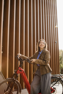 Korean woman pauses beside her electric bike in warm light