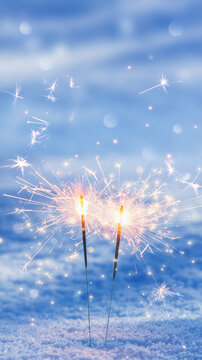 two burning sparklers isolated in snow with copy space on blurred background, social media format for christmas, new years eve or valentines day