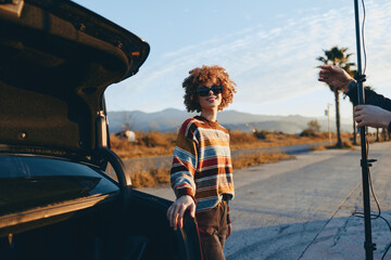 Child stands by car door on rural road, outdoors travel lifestyle, sunny desert landscape, curly...