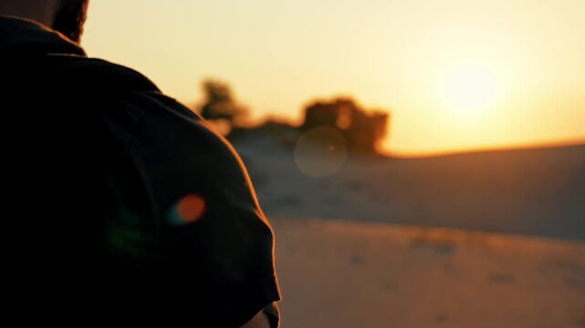 Young man walking at sunset with golden sunlight shining on his shoulders. Warm sun rays highlight his silhouette in the evening light.