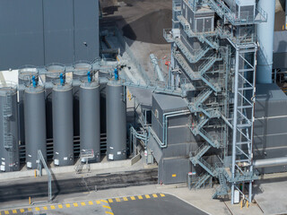 Tall grey industrial silos with access ladders and connecting pipes alongside a steel asphalt mixing tower with multiple maintenance stairs at a road materials manufacturing facility in Sydney © Paul Tama