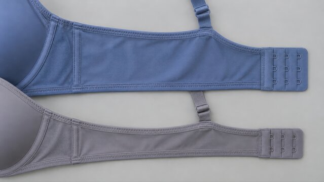 Narrow grey and broader dusty blue rear bra bands lie parallel on a consultation mat for comparing everyday garment construction before a retail fitting appointment