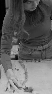 A woman carefully shapes a lump of raw wool fibers at a cluttered table