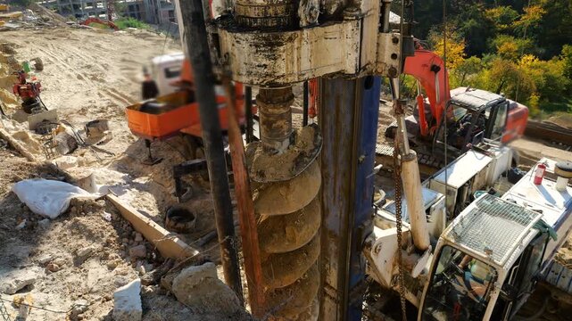 A drilling rig operates at a construction site to install bored piles as heavy hydraulic crawler equipment drills into the soil while an excavator assists with deep foundation works on a autumn day.