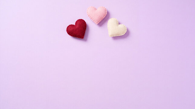 Three colorful handmade felt hearts displaying symbols of love, care, and romance arranged on a soft purple surface
