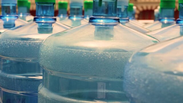 Large plastic water jugs with condensation sit together in a sunlit row