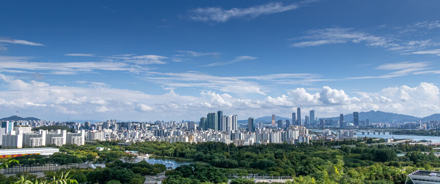 Panoramic view of modern Asian metropolis skyline with skyscrapers, park, and river under cloudy sky   