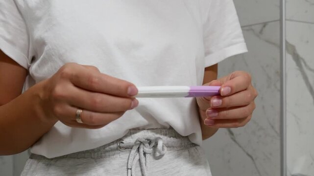 Close-up of woman holding pregnancy test and checking result in bathroom, pregnancy and family planning concept